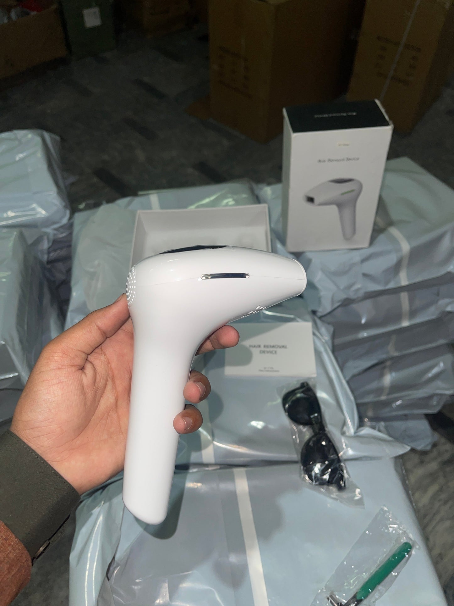 Hand holding a white handheld device with packaging and accessories in the background